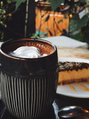 Hot chocolate in a cup with coconut cream and with raw dessert, outdoor, green background, top view. passion fruit cake. closeup. coconut cream. raw dessert. natural. mobile photography. 
