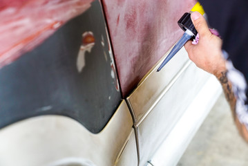 car mechanic using a pneumatic putty gun to glue car parts before a paint job in the body shop