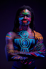 portrait of african man painted in fluorescent paint on face and shirtless muscular torso, studio shot with UV light.