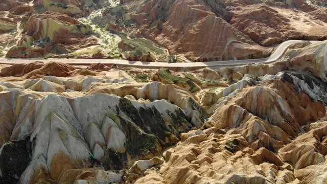 Top Aerial View of Rainbow Mountains Geological Park. Stripy Zhangye Danxia Landform Geological Park in Gansu Province, China. Flying Drone Picture of Tourist Buses on a Road in Valley on a Sunny Day.