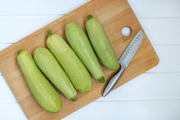 Fresh green zucchini on a chopping Board next to a knife on a white wooden background. The view from the top. Space for text. Healthy food and food for vegetarians.