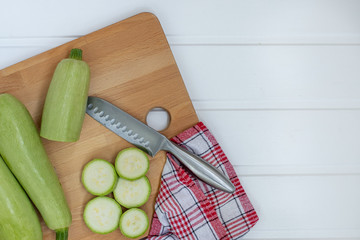 Fresh green zucchini on a chopping Board next to a knife on a white wooden background. The view from the top. Space for text. Healthy food and food for vegetarians.