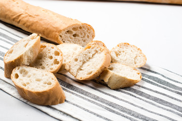 French baguette bread cut into slices. White towel kitchen with gray lines.