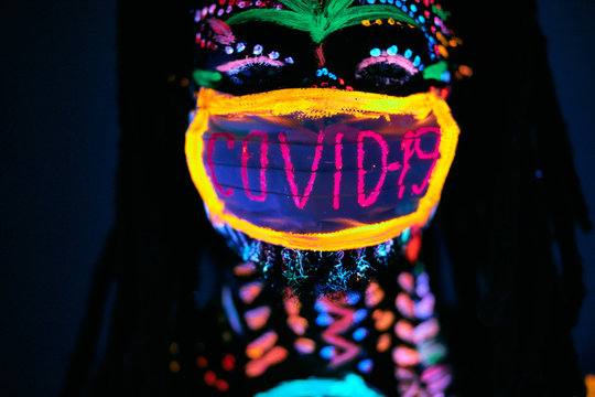 close-up photo of young male in fluorescent mask COVID-19, inscription glows on neon lights, body art. epidemic, pandemic coronavirus concept