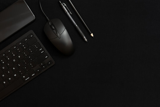 Black smartphone, black keyboard, black pencil, black pen and black computer mouse on a black background. Business items. Low key photo. Free space for text. Dark on dark.