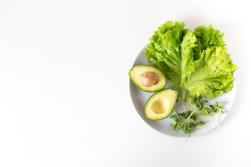 Vegan detox plate with green vegetables. Raw avocado, salad, micro greens on white background. Top...