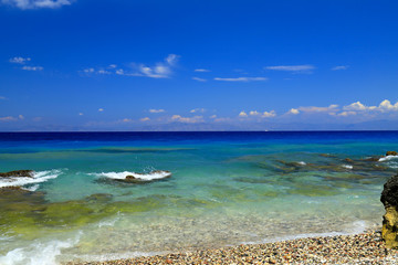 Picturesque summer beach, pebbles in the clear transparent water, Rhodes, Greece, Blue flag beach, island for travel, leisure. Sea background, summer vacation.