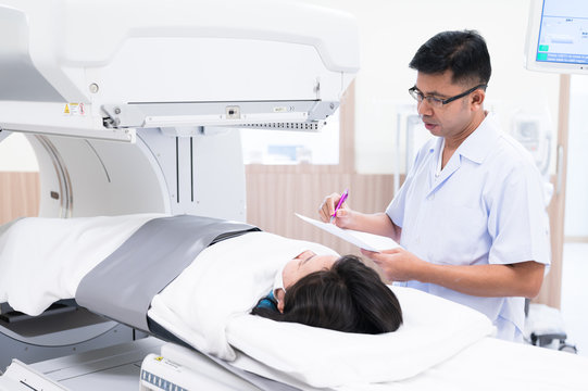 Asian radiologists explain treatment information to patients in x-ray room.CT (Computed tomography) scanner machine.High technology medical treatment equipment concept.