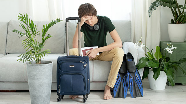 Sad tourist teen with a suitcase and flippers stays at home during the coronavirus pandemic. Cancellation of leave and closing of borders between countries. Flight cancellation