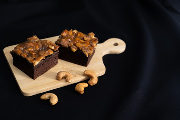  The square slice of toffee cake with cashew nut
and caramel syrup on wooden plate ,black background