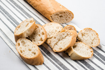French baguette bread cut into slices. White towel kitchen with gray lines.