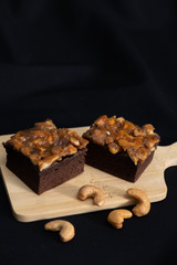  The square slice of toffee cake with cashew nut
and caramel syrup on wooden plate ,black background