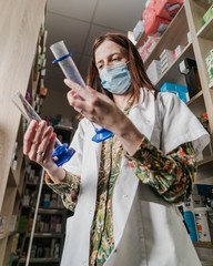Pharmacist working during a coronavirus pandemic in pharmacy store and preparing medicines. Wearing a protective mask. Pharmacist looking for a medicines to give to ill person.