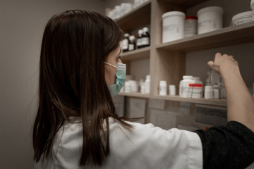 Tired pharmacist working during a coronavirus pandemic and wearing an anti-virus mask. Pharmacist looking for a medicines.