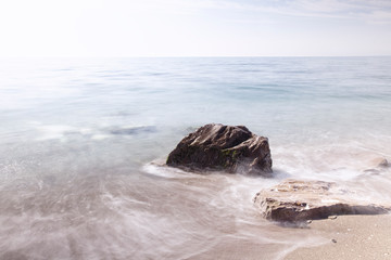 mar en calma con una gran roca sobre la arena y el horizonte al fondo 