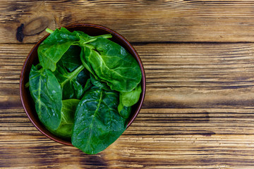 Ceramic bowl with spinach leaves on rustic wooden table. Top view
