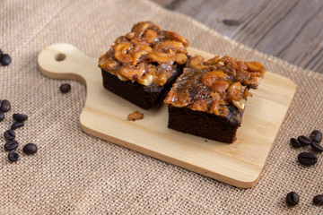 The square slice of toffee cake with cashew nut and caramel syrup on sackcloth and wooden table.