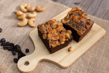 The square slice of toffee cake with cashew nut and caramel syrup on sackcloth and wooden table.