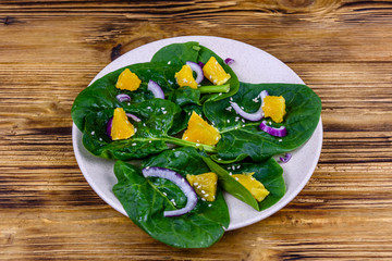 Salad with spinach leaves, pieces of orange, sesame seeds and onion in a ceramic plate