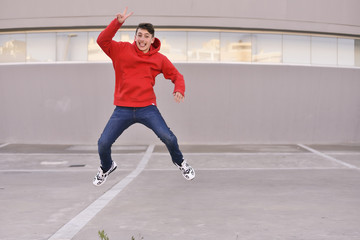 Fototapeta premium Smiling young man in red clothing jumping for joy in front of his workplace. Happy concept for getting a job. Free space