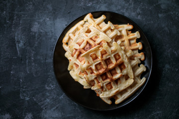 Viennese homemade waffles on a black plate and a dark background, top view, there is a place for text or description
