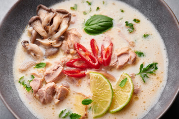 Tom Kha Gai or Thai Coconut Chicken Soup in matte gray bowl on concrete backdrop. Tom Kha Gai is Thailand cuisine dish with coconut milk, chicken, galangal, lemongrass, mushrooms, lime. Thai Food