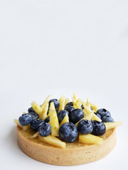 French dessert. Tart with blueberries, pineapple and lime zest. White background. Back view. There is a copy space for your text.