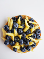 French dessert. Tart with blueberries, pineapple and lime zest. White background. Top view. 