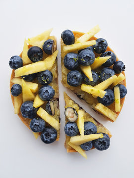 French Dessert. Sliced Tart With Blueberries, Pineapple And Lime Zest. White Background. Top View.