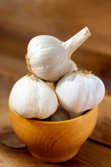 Fresh ripe garlic in wooden bowl, on wooden background. Cooking ingredient.