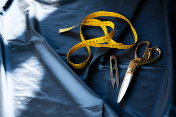 Close-up of sewing supplies. Scissors, wire cutters, an orange measuring tape lie on a fabric table.