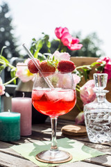 Strawberry Cocktail on a wooden table in the sun with flowers and candles