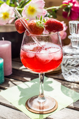 Strawberry Cocktail on a wooden table in the sun with flowers and candles