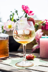 Cocktail on a wooden table in the sun with flowers and candles