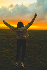 Young woman jumping in green field on the sunset. Beautiful girl on the nature