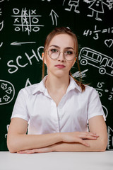 Young teacher is sitting near blackboard in classroom