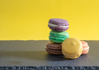 Group of five macaroons of different colours arranged on top of each other with a plain coloured background