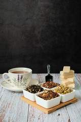 Detail of a mug with red tea, dry tea leaves and wafer biscuits. Copy space with dark background