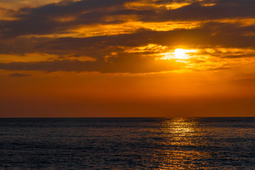 Obraz premium Beautiful sunset on the sea. The rays of the setting sun Shine through the clouds in the orange sunset sky. A luminous path from the sun on the sea surface.