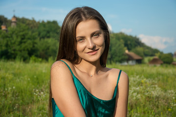 Beautiful young woman in a green dress is smiling at the rural landscape background
