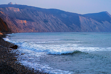 Storm and waves on the Black sea. A wave rolls over the rocky beach. In the background, the mountains are illuminated by the setting sun.