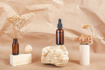 Serum or essential oil in brown glass bottle with pipette on stone, wooden geometric shapes and dried flowers on beige paper background. Natural Organic Spa Cosmetic concept Front view
