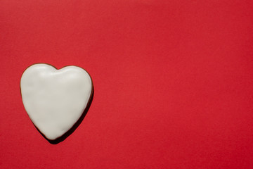 Fototapeta premium Pretty handmade gingerbread cookie covered with icing on the bright red background. Romantic banner. Copy space. Top view.