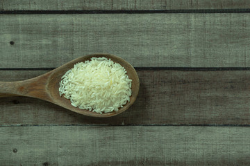 Uncooked dry Thai jasmine rice in wooden ladle isolated on wood floor, angle of view flat lay and top down horizontal view.