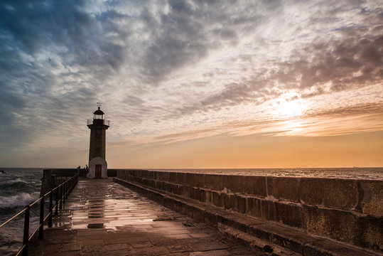 Paisaje marino: puesta de sol sobre el dique que lleva al faro con nubes altas en el cielo