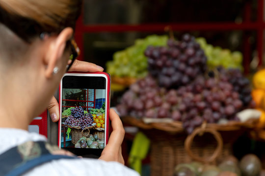 Exotic fruits on the counter and on the screen of the phone in the hands of a girl. The image of the girl is cut off. Selective focus.
