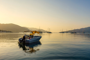 Fototapeta premium Small boat at dawn in the sea. In the distance mountains and boats