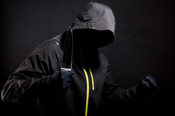 Fototapeta premium Unknown, indistinguishable bandit in black with knife attacks the victim. Concept: Crime because of crisis covid 19. Isolated on black background. Selective focus
