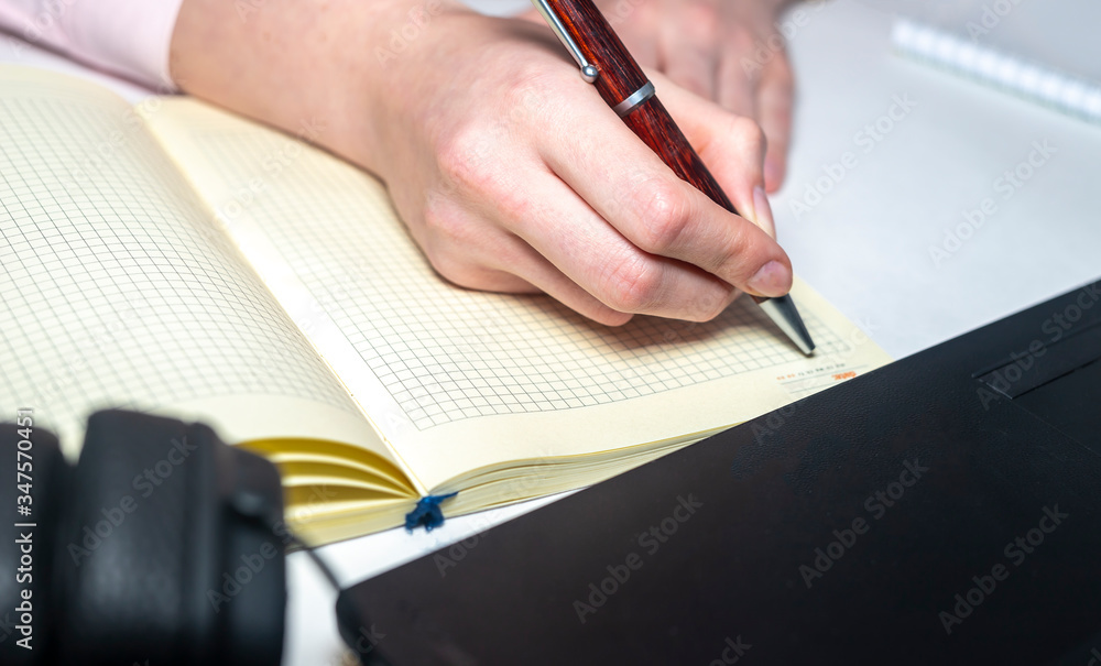 Poster female hands is writing smth on notebook with laptop notebook pen around on white table. online busi