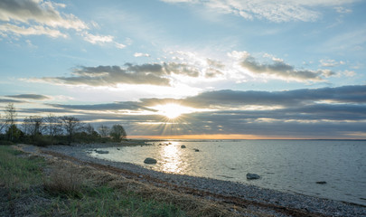 Southern coast of the Finnish Gulf. Rocks covered with green seaweed in the Baltic sea. Smooth transparent reflective water. Orange sunset markings under the low altitude clouds. Estonia, Baltic